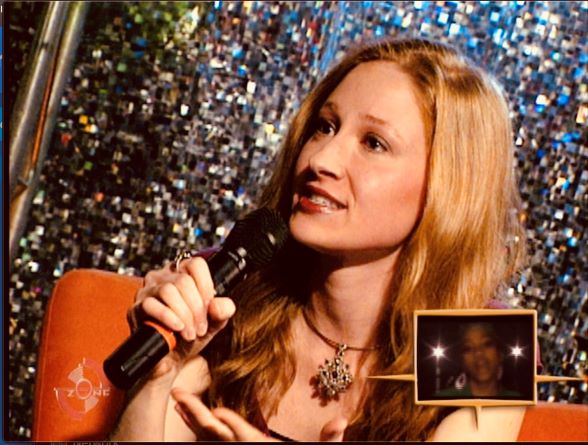 Bekka seated in a chair and speaking into a hand-held mic during an interview.