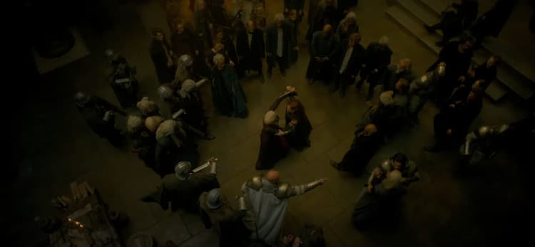 Overhead shot of two fighters, Rhaenyra and Alicent, locked in hand-to-hand combat and surrounded by a crowded circle of people, most in armor.