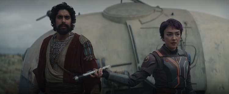 Sabine tries to hand Ezra a lightsaber, standing in front of a Noti mobile home