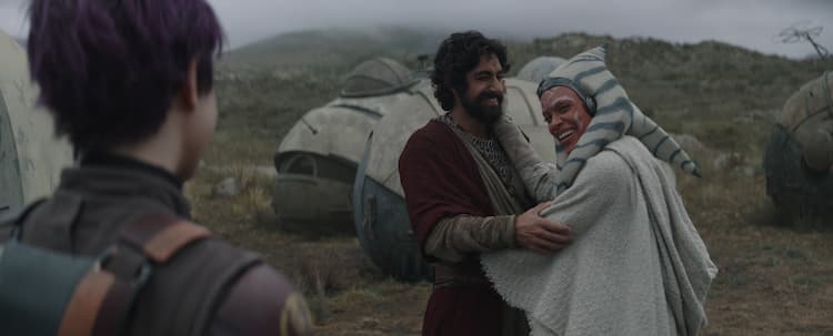 Ezra and Ahsoka hug and smile while Sabine looks on in the foreground.