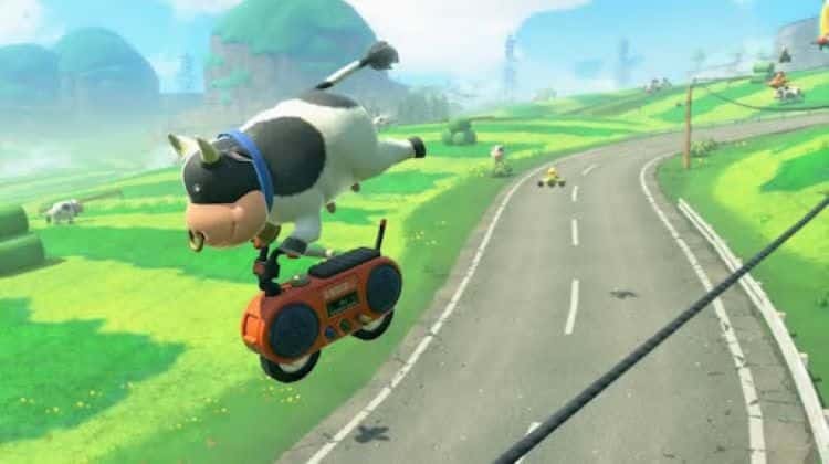 A cow is doing tricks on a motorbike while grinding on a power line. They are racing through Moo Moo Meadows. Another racer and normal cow are in the background. Several trees are in the distance.